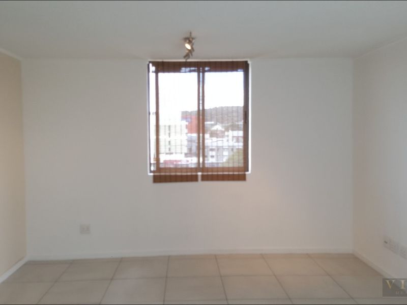 A bright, empty bedroom featuring neutral tiled flooring, a central ceiling light, and a window fitted with blinds.