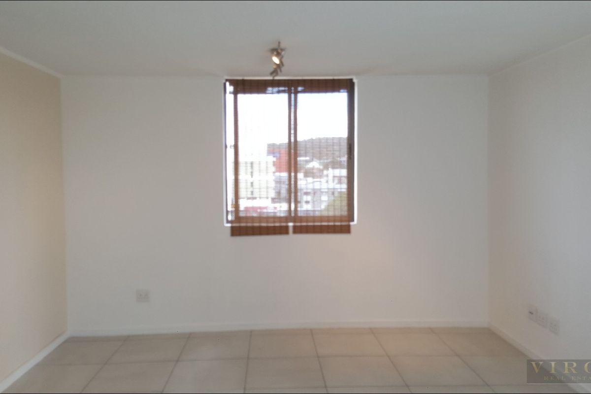 A bright, empty bedroom featuring neutral tiled flooring, a central ceiling light, and a window fitted with blinds.