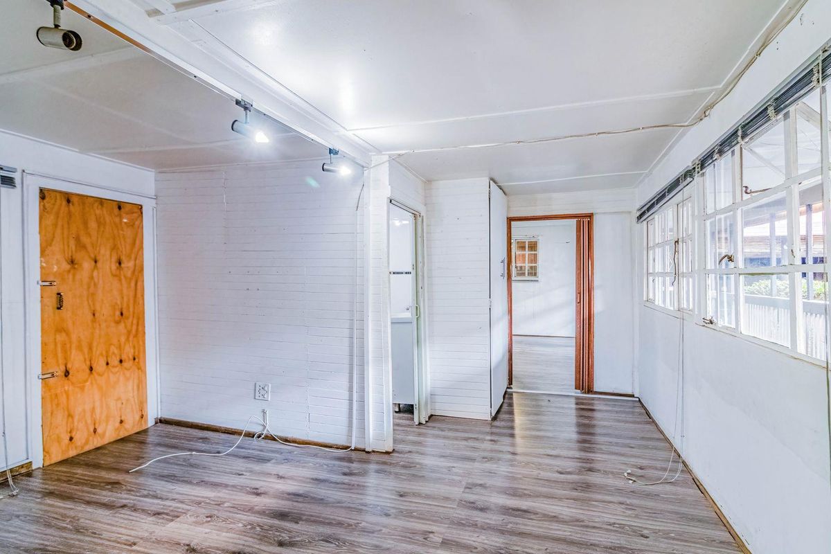 An empty living area featuring wood-look laminate flooring, white panelled walls, track lighting, and multiple access points to adjacent rooms.
