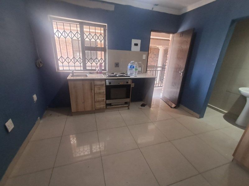 A compact kitchen area featuring tiled floors, a built-in oven and hob, and a stainless steel sink, with direct access to an outdoor area.