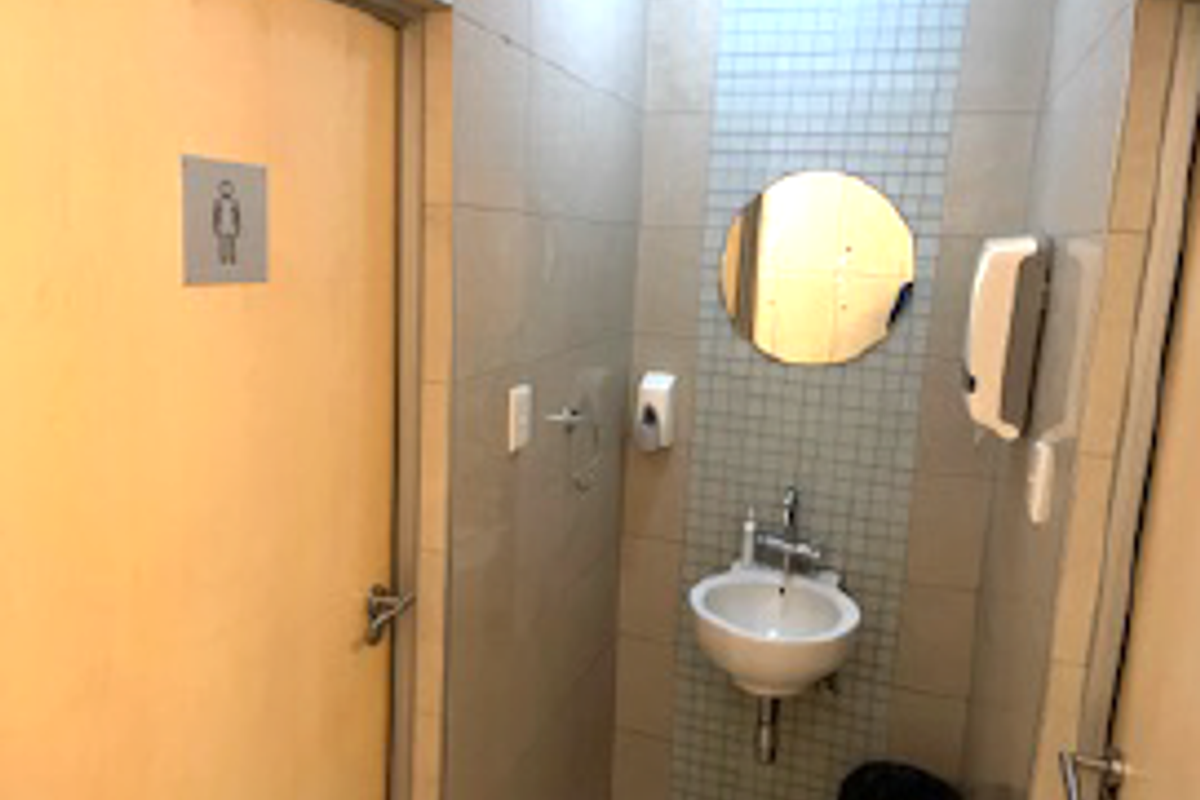 A compact commercial restroom featuring tiled walls, a wall-mounted basin, a circular mirror, and a soap dispenser.
