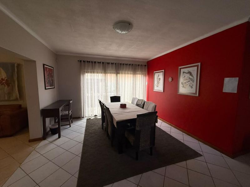A dining room featuring tiled flooring and a sliding glass door providing natural light, with a bold red accent wall.