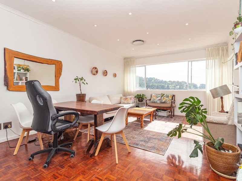 A bright and spacious living area featuring warm parquet flooring, recessed lighting, and a large window offering natural light and scenic views.