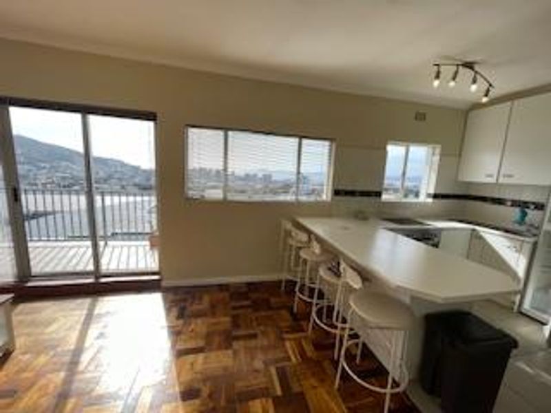 Open-plan kitchen and living area featuring parquet flooring, a breakfast bar, and sliding doors leading to a balcony with scenic views.