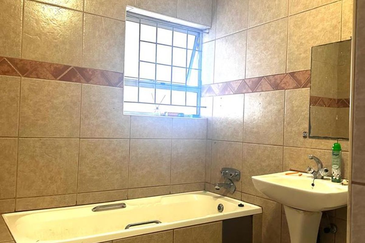 A dated bathroom featuring a built-in bathtub, pedestal basin, and full-height wall tiling, requiring cosmetic updates to the ceiling and finishes.