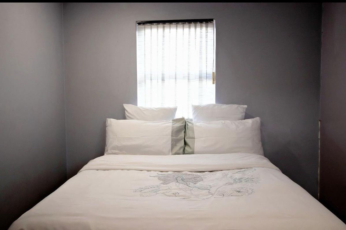 A simple bedroom featuring grey walls and a window with vertical blinds, providing a neutral and functional sleeping space.
