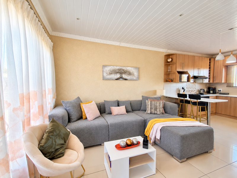 A bright open-plan living and kitchen area featuring tiled floors, a modern breakfast bar, and integrated cabinetry with a clean, functional layout.