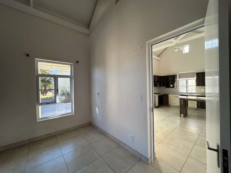 An open-plan living area featuring high vaulted ceilings, tiled flooring, and a view into a modern kitchen with built-in cabinetry and an island.