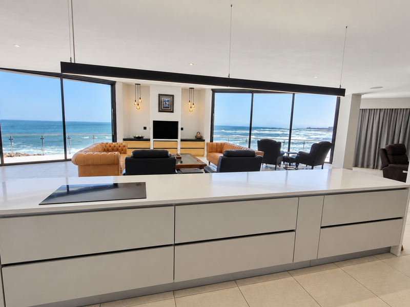 Spacious open-plan living area featuring a modern kitchen island with induction cooktop, floor-to-ceiling glass doors, and panoramic ocean views.