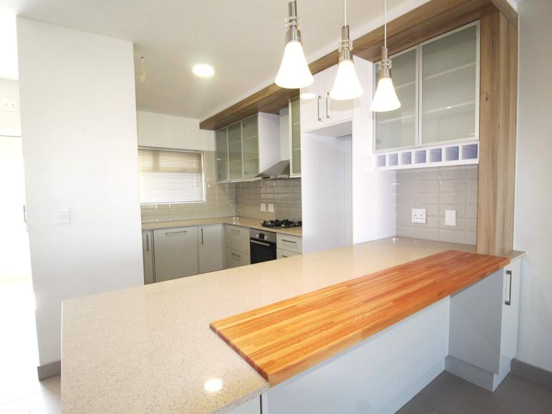 Modern kitchen featuring sleek cabinetry, stone countertops, a wooden breakfast bar, built-in oven, gas hob, and stylish pendant lighting.