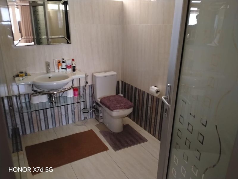 A functional bathroom featuring a wall-mounted basin, toilet, and tiled finishes, accessible via a frosted glass door.