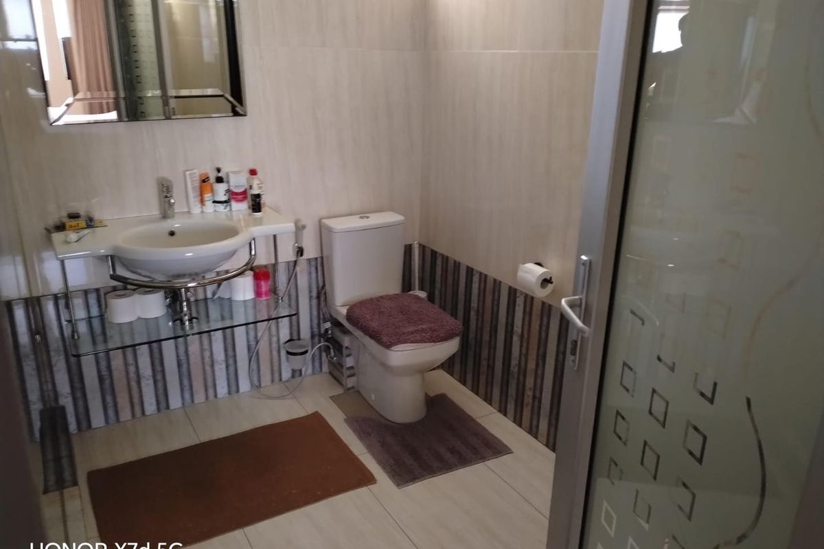 A functional bathroom featuring a wall-mounted basin, toilet, and tiled finishes, accessible via a frosted glass door.