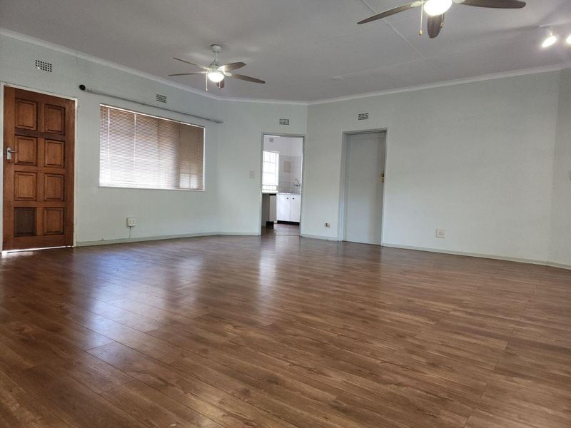 Spacious, empty living area featuring laminate flooring, ceiling fans, and neutral walls, providing a versatile blank canvas for interior design.