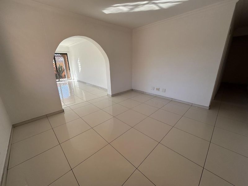 A bright, empty living area featuring neutral tiled flooring and a distinctive architectural archway leading to an adjacent space.