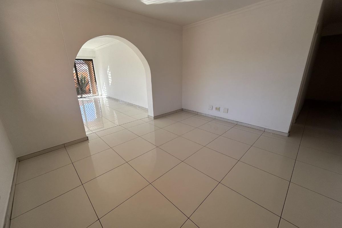 A bright, empty living area featuring neutral tiled flooring and a distinctive architectural archway leading to an adjacent space.