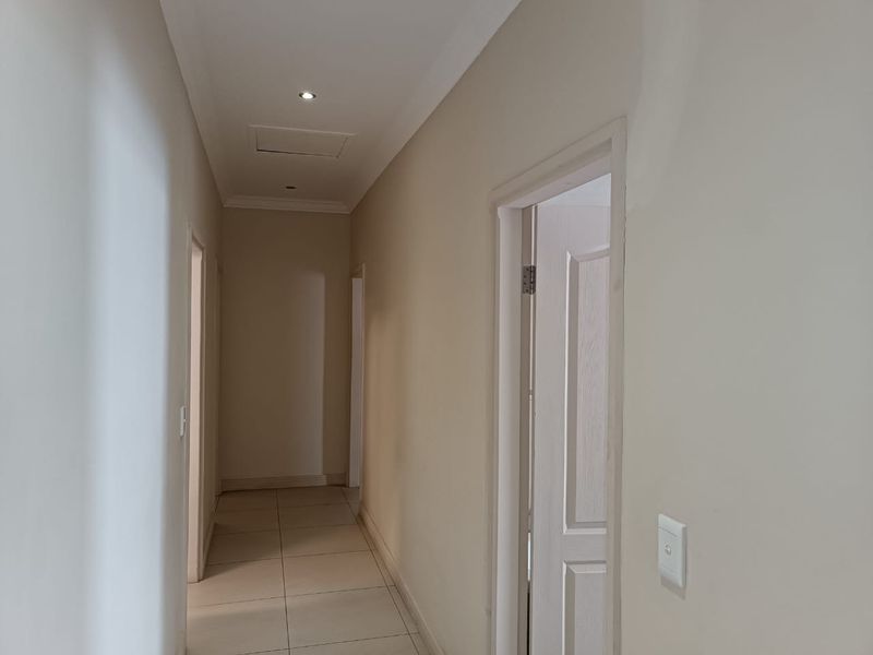 A clean, neutral-toned hallway featuring tiled flooring, recessed downlighting, and a ceiling access hatch, providing access to multiple rooms.