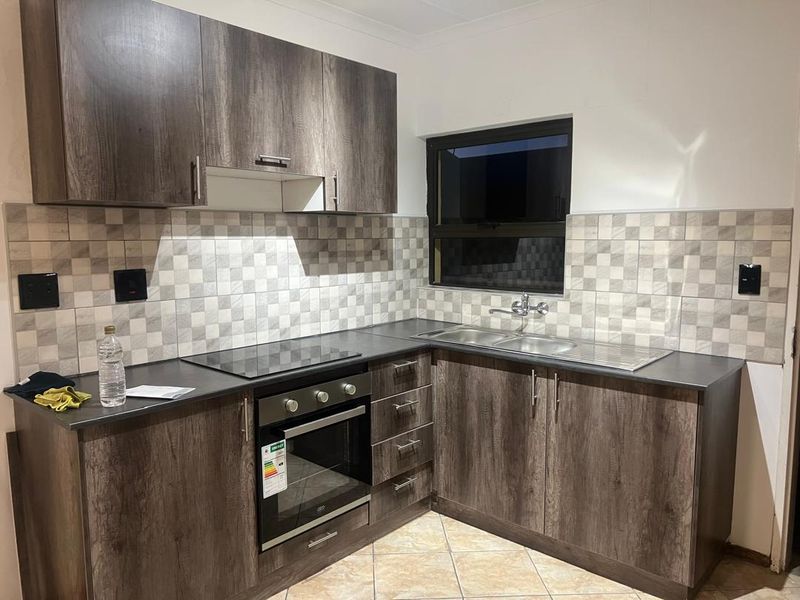 Modern kitchen featuring dark wood-look cabinetry, laminate countertops, a built-in oven with electric hob, and a double sink with tiled backsplash.