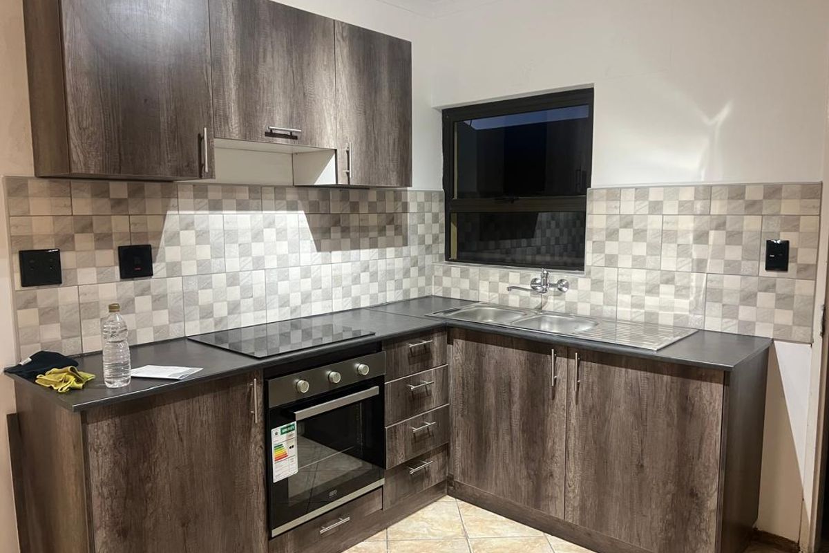 Modern kitchen featuring dark wood-look cabinetry, laminate countertops, a built-in oven with electric hob, and a double sink with tiled backsplash.