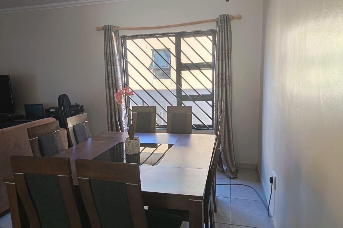 A dining area featuring tiled flooring and a window fitted with security bars, providing a functional space for family meals.