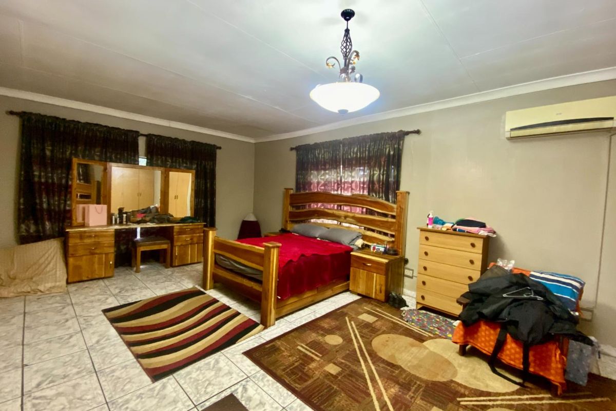 Spacious bedroom featuring tiled flooring, a wall-mounted air conditioning unit, and a central pendant light fixture.