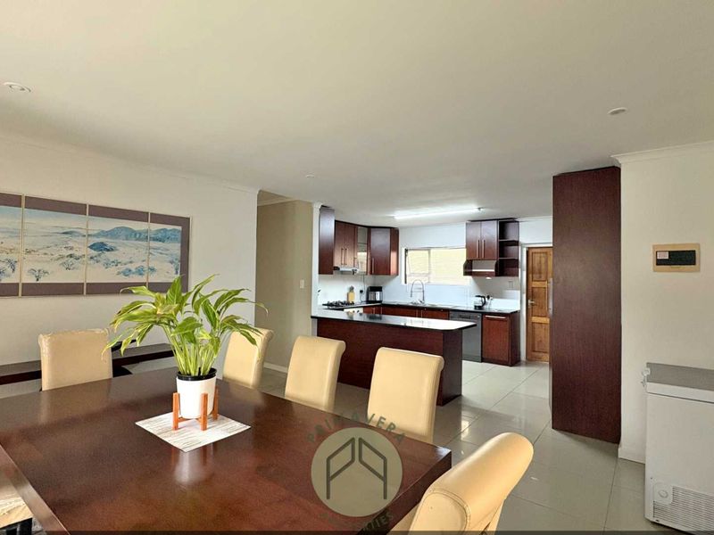 Open-plan living and dining area featuring a functional kitchen with dark wood cabinetry, a breakfast island, and tiled flooring throughout.