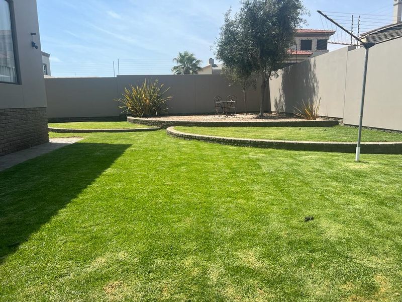 A well-maintained rear garden featuring tiered lawn levels, stone retaining walls, and perimeter boundary walls.