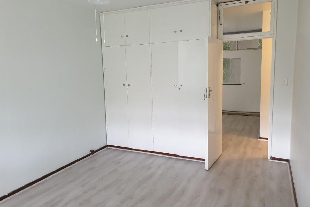 A bright, empty bedroom featuring modern light-toned laminate flooring, floor-to-ceiling built-in cupboards, and a ceiling fan.