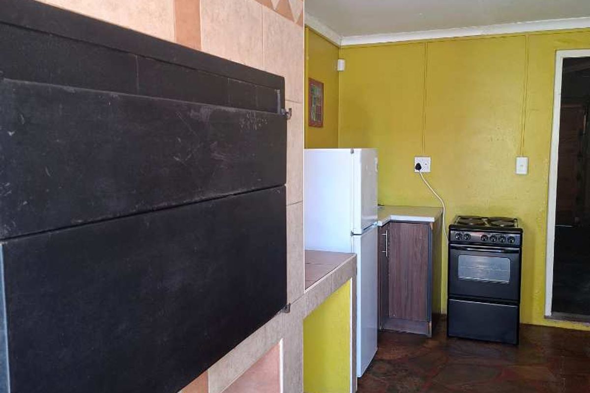 Kitchen area featuring a built-in braai, tiled flooring, and a freestanding stove, offering a functional space with potential for modern updates.