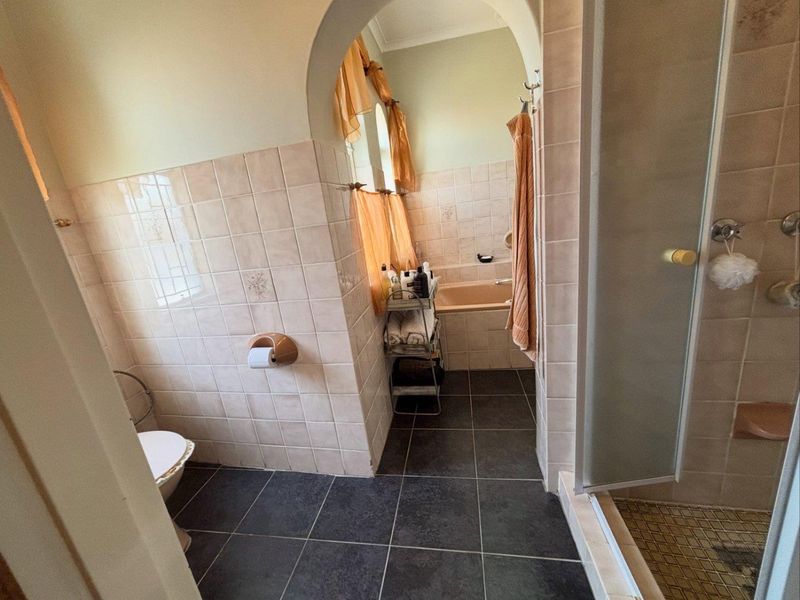 A dated bathroom featuring a separate shower enclosure, built-in bathtub, and tiled finishes throughout, connected by a distinctive arched doorway.