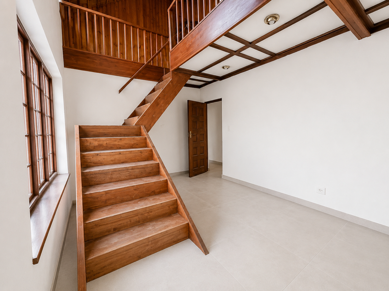 Spacious living area featuring a prominent wooden staircase, mezzanine level with timber railing, exposed ceiling beams, and large timber-framed windows.