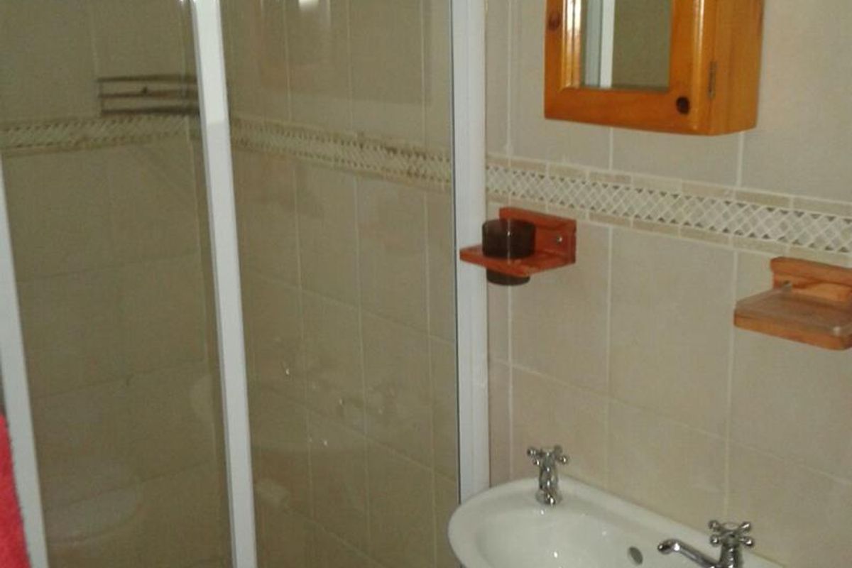 Compact bathroom featuring a shower enclosure with pebble flooring, wall-mounted basin, and tiled walls with decorative border.