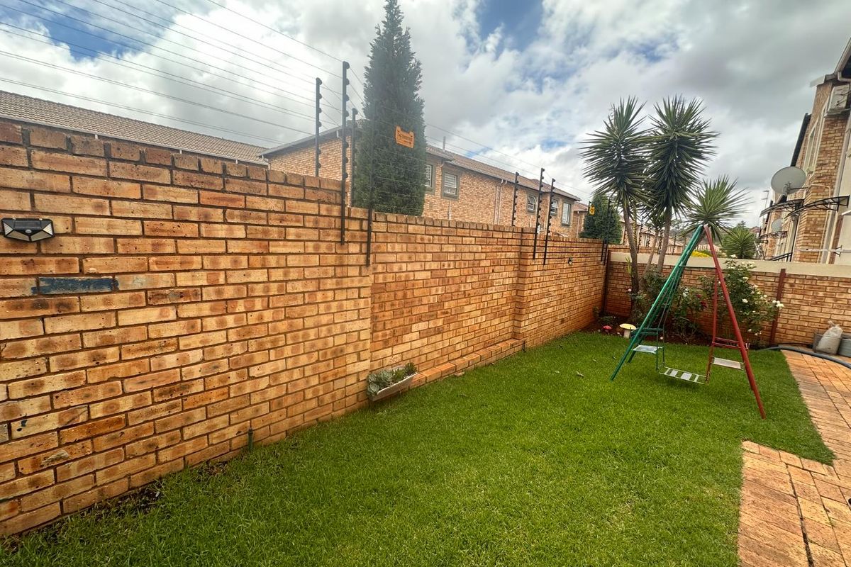 A private rear garden featuring a well-maintained lawn, paved walkway, and secure brick boundary wall topped with electric fencing.