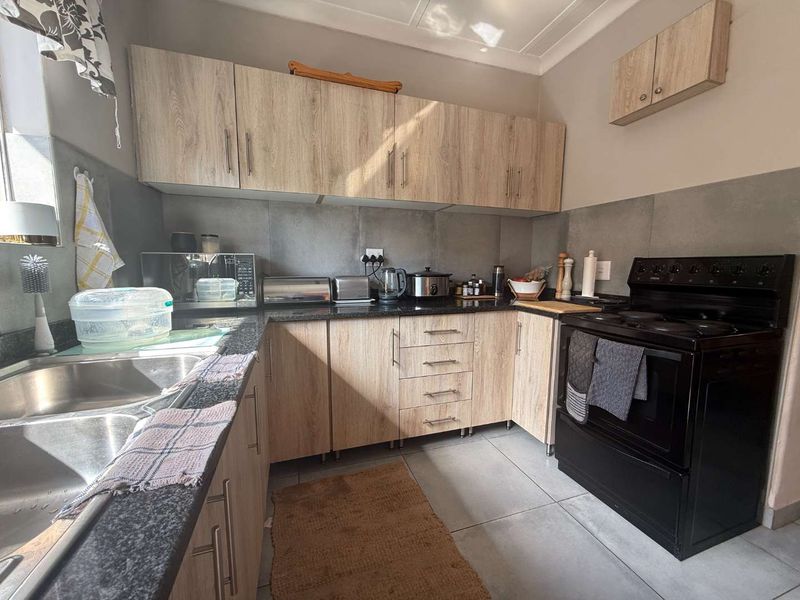 A functional kitchen featuring light wood-look cabinetry, dark granite countertops, a stainless steel double sink, and a freestanding electric stove with tiled backsplash.