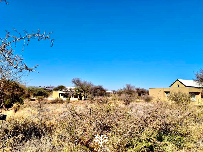 A view of a residential property set within a natural, undeveloped landscape with dry vegetation and clear blue skies.