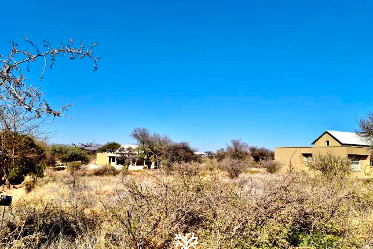 A view of a residential property set within a natural, undeveloped landscape with dry vegetation and clear blue skies.