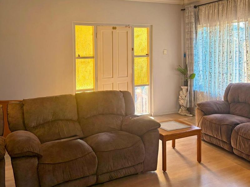 A comfortable living room featuring laminate flooring, recessed downlighting, and a classic timber-framed front entrance with decorative sidelights.