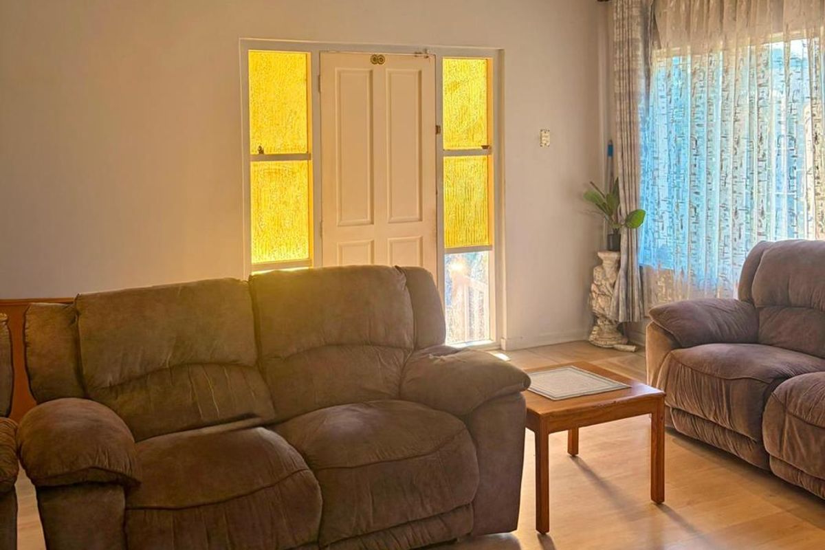 A comfortable living room featuring laminate flooring, recessed downlighting, and a classic timber-framed front entrance with decorative sidelights.