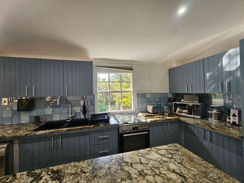 A functional kitchen featuring blue cabinetry, granite countertops, a gas hob, built-in oven, and a tiled backsplash with a garden-facing window.