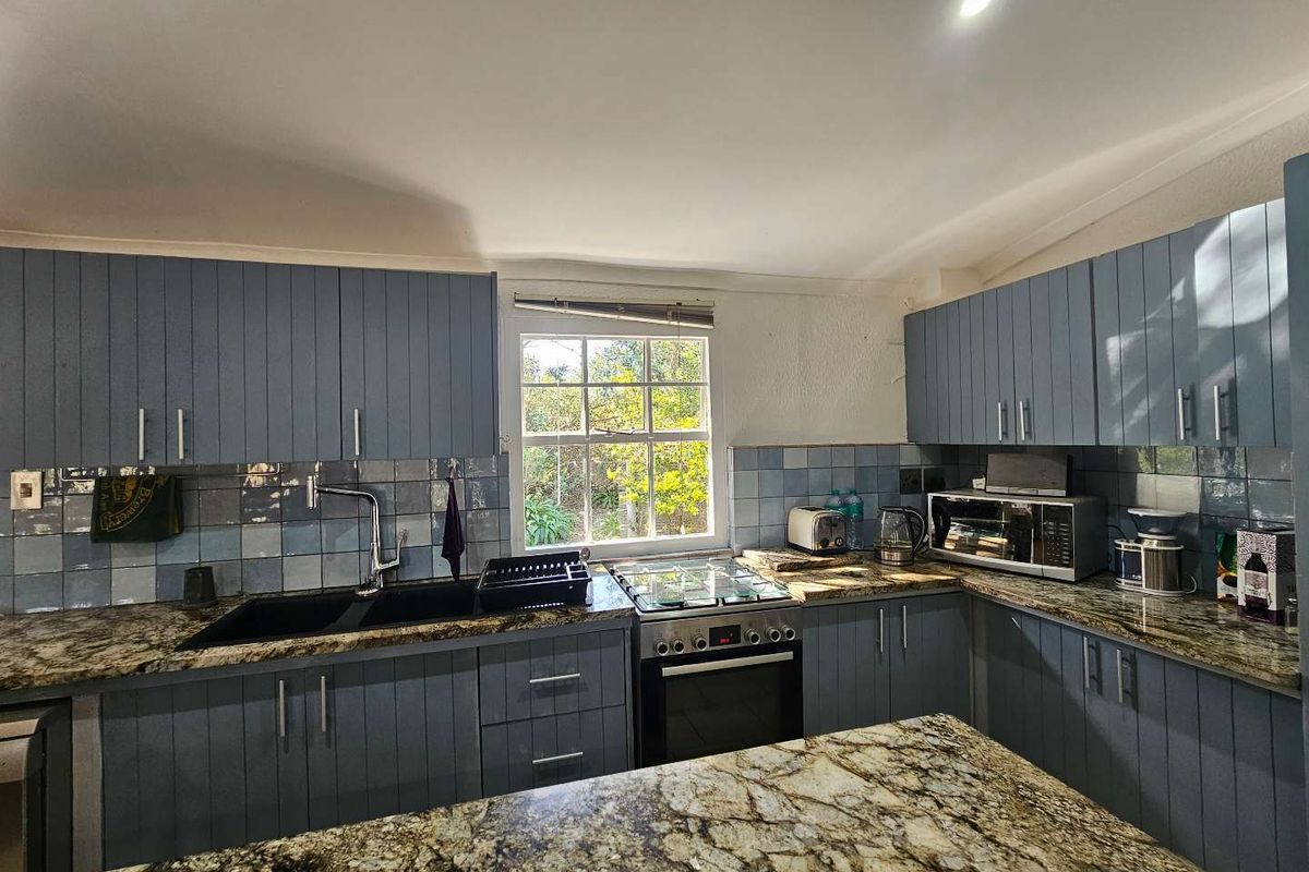 A functional kitchen featuring blue cabinetry, granite countertops, a gas hob, built-in oven, and a tiled backsplash with a garden-facing window.