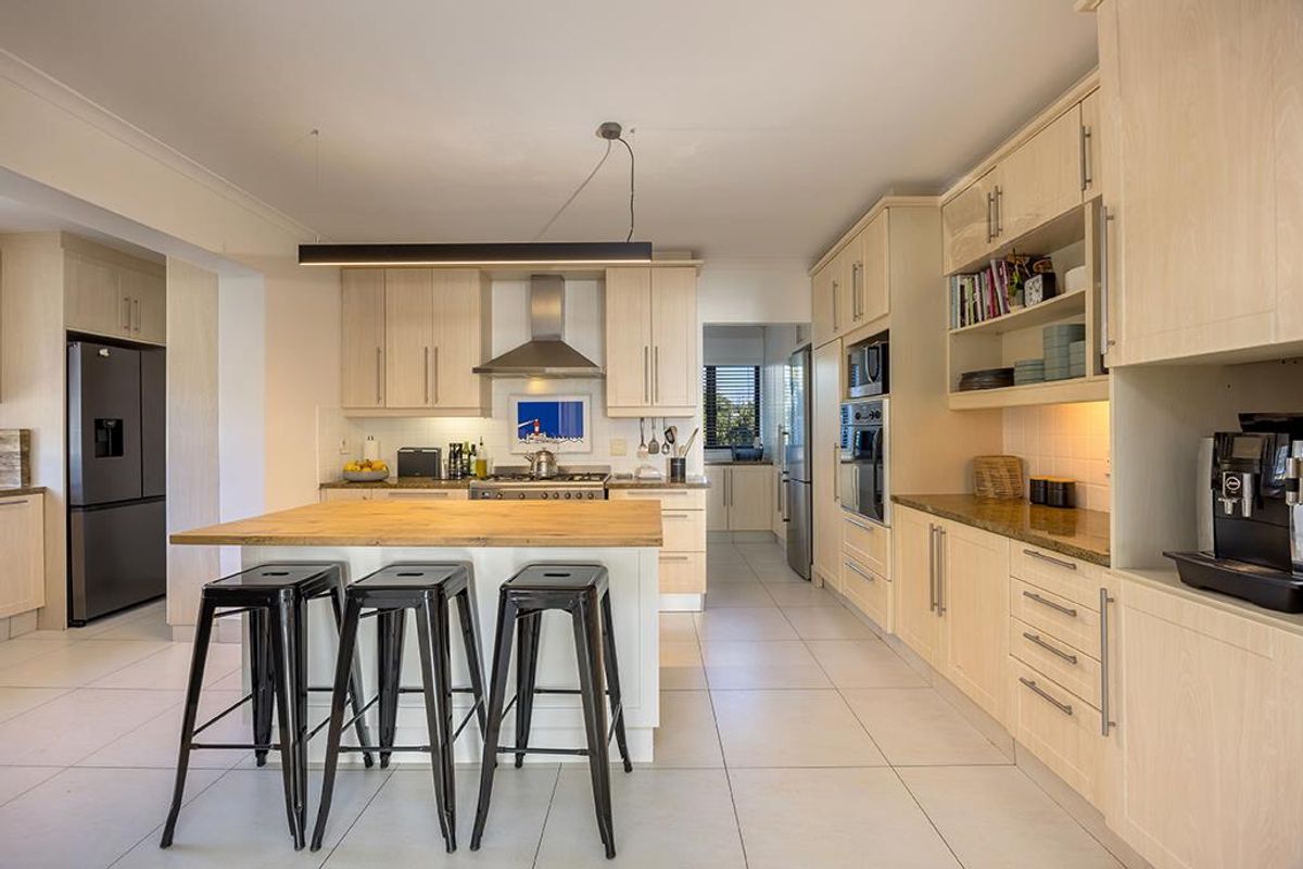 Modern kitchen featuring light wood cabinetry, stone countertops, a central island with breakfast bar seating, and integrated stainless steel appliances.