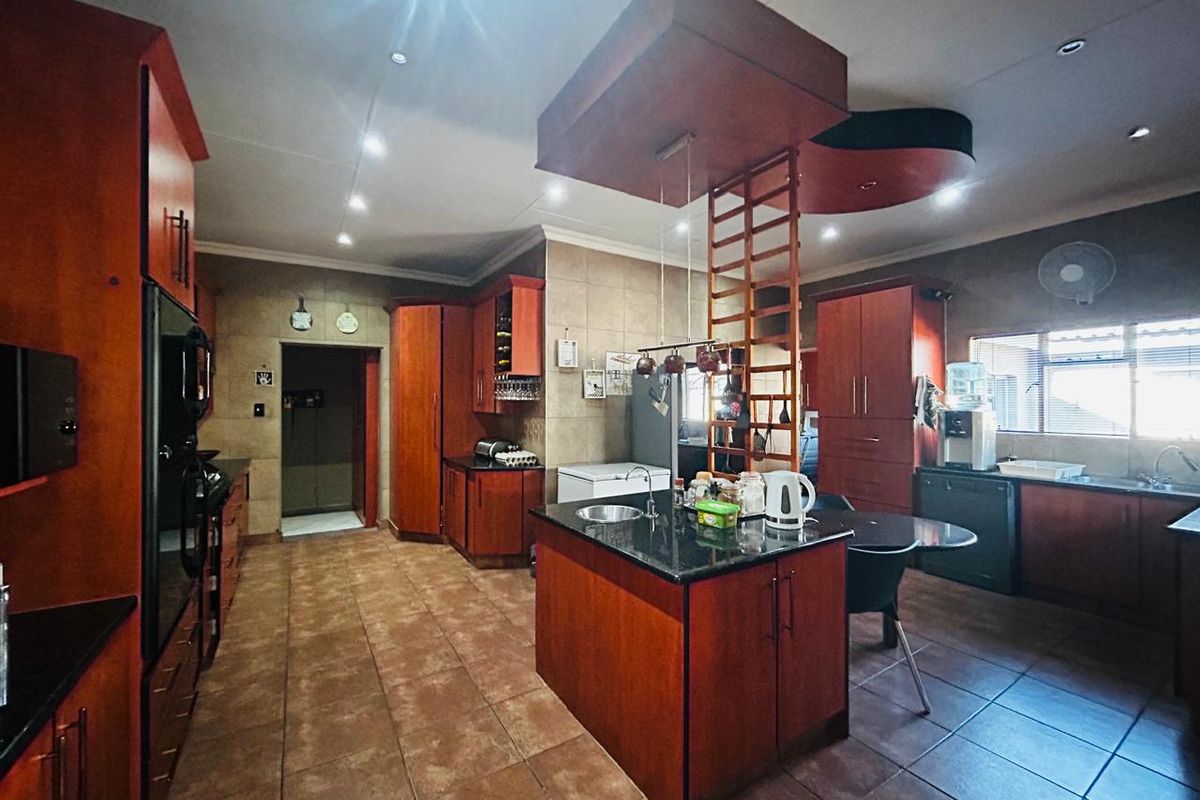 Spacious kitchen featuring dark wood cabinetry, granite countertops, a central island with a prep sink, and tiled flooring throughout.
