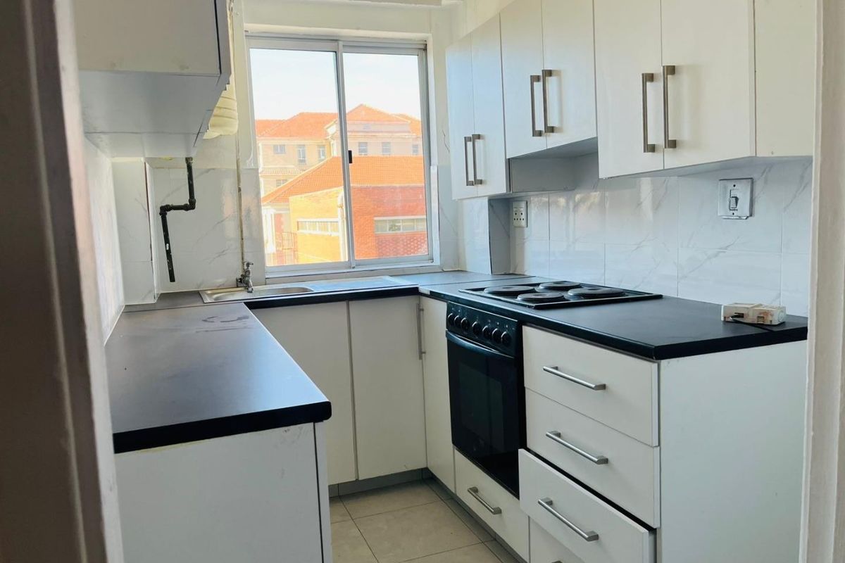Compact kitchen featuring white cabinetry, black countertops, built-in oven and stove, and tiled finishes.