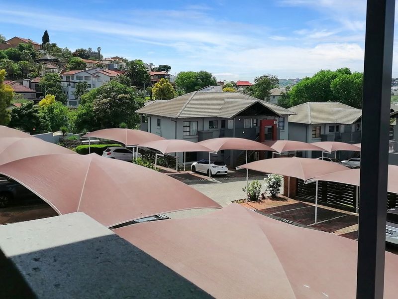 Elevated view overlooking the townhouse complex parking area featuring multiple shade cloth carports and surrounding residential landscape.