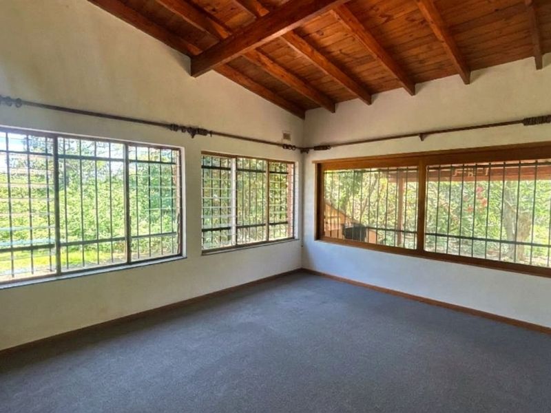 Spacious living area featuring exposed timber ceiling beams, carpeted flooring, and large windows with security bars, offering plenty of natural light.