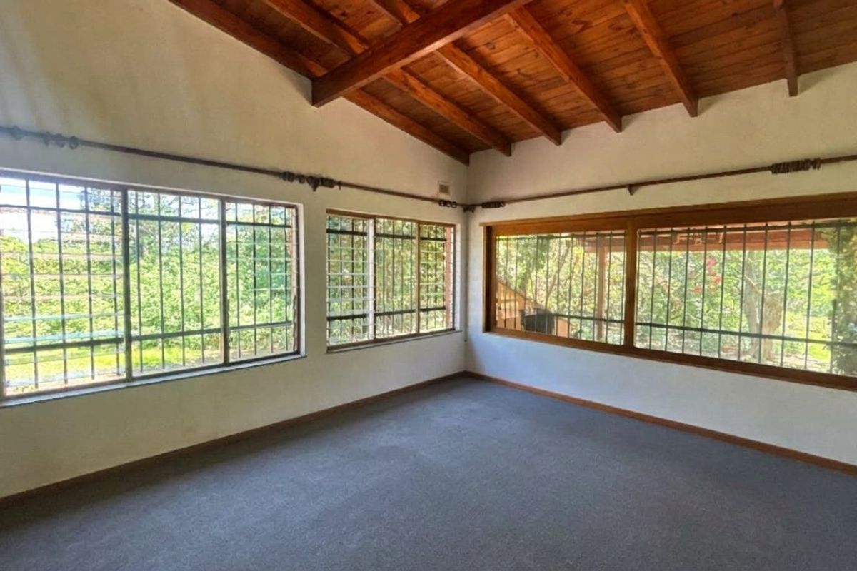 Spacious living area featuring exposed timber ceiling beams, carpeted flooring, and large windows with security bars, offering plenty of natural light.