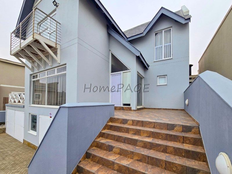 Front elevation of a multi-level house featuring a tiled staircase, balcony with metal railing, and paved driveway access.