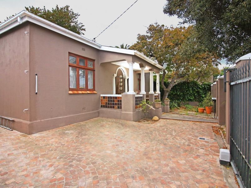 Front elevation of a cottage featuring a brick-paved driveway, covered porch with decorative columns, and secure perimeter fencing.