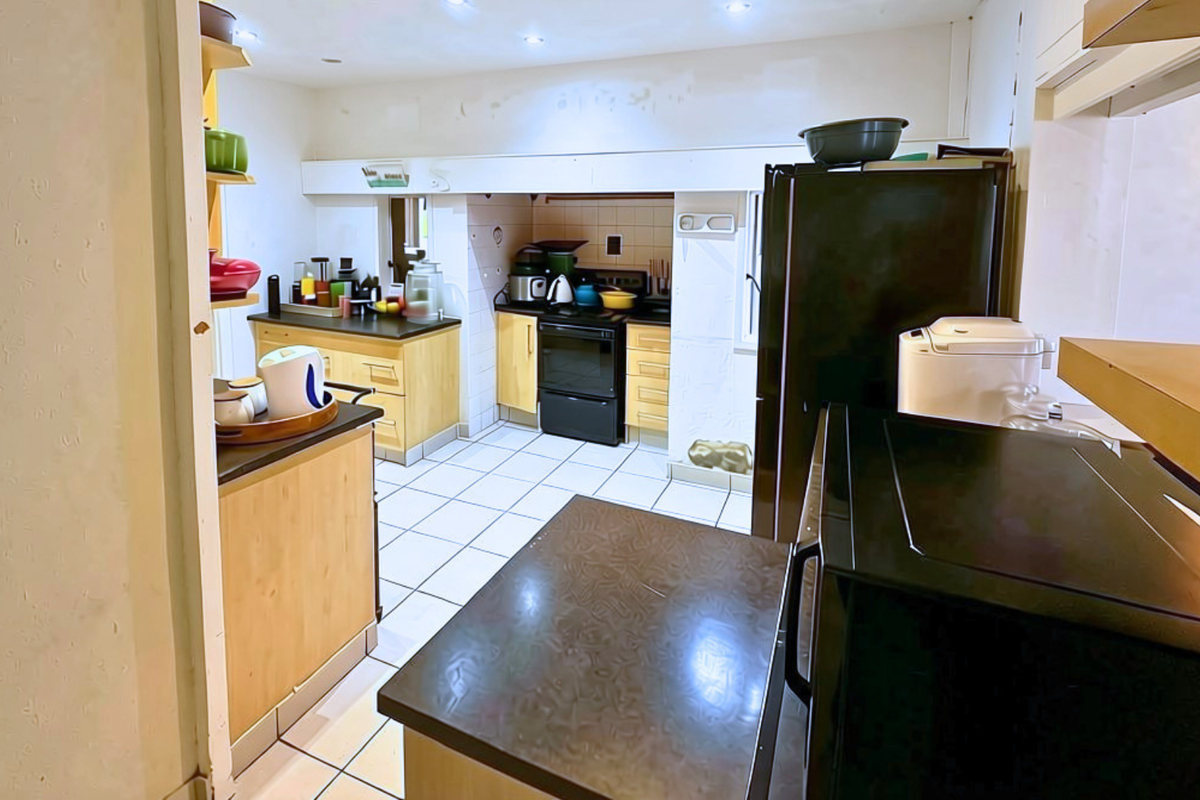 A functional kitchen featuring tiled flooring, built-in wooden cabinetry, and a black electric stove, offering a practical layout for daily meal preparation.