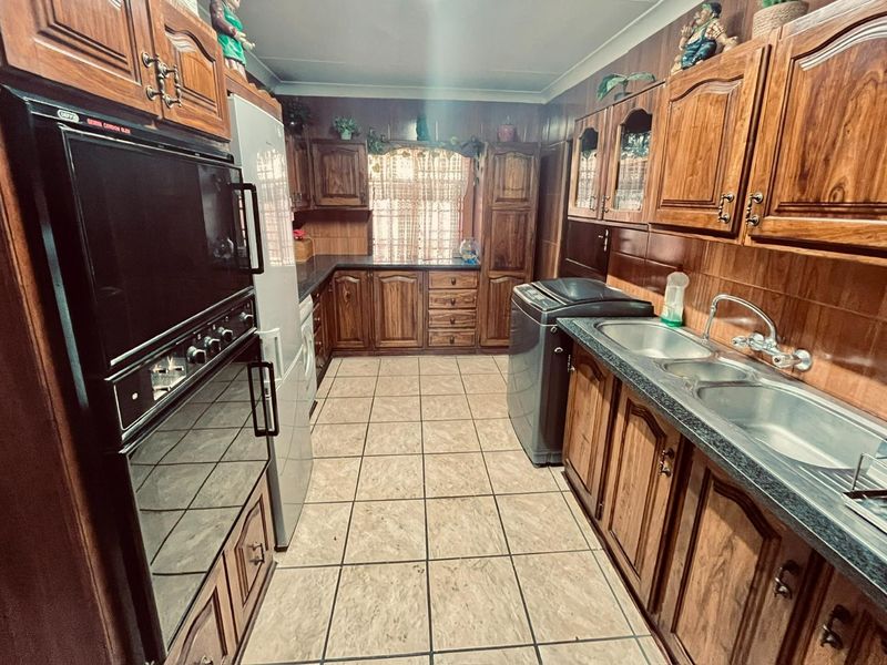 A functional kitchen featuring extensive wooden cabinetry, a double bowl sink, and a built-in eye-level oven with tiled flooring throughout.