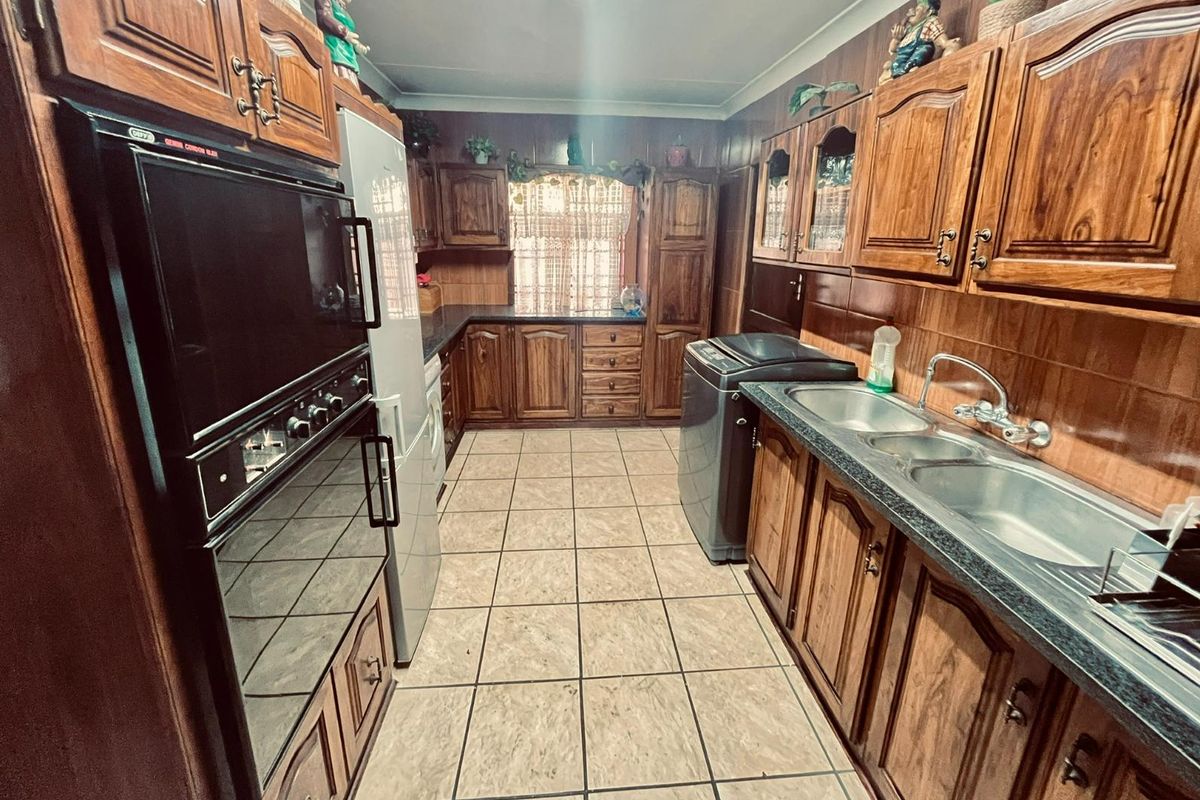 A functional kitchen featuring extensive wooden cabinetry, a double bowl sink, and a built-in eye-level oven with tiled flooring throughout.
